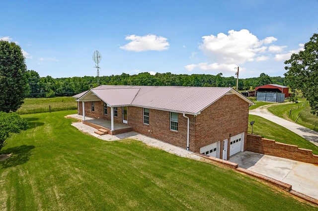 back of house with driveway, a garage, metal roof, a yard, and brick siding