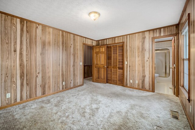 unfurnished bedroom featuring ornamental molding, wood walls, carpet, and a closet