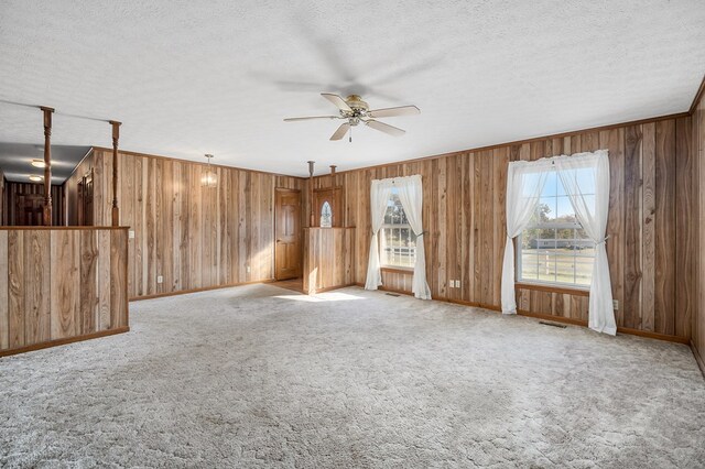 unfurnished room featuring light carpet, visible vents, a ceiling fan, a textured ceiling, and wood walls