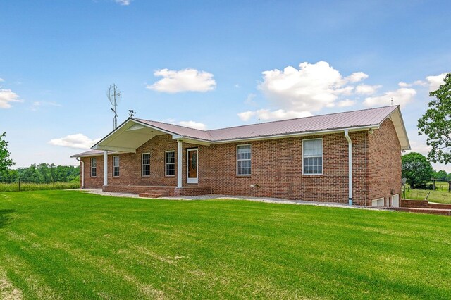 rear view of property featuring a yard, brick siding, and metal roof