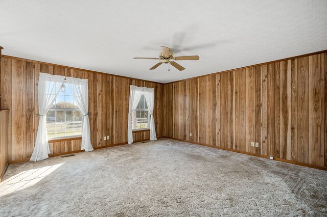 empty room featuring visible vents, light carpet, wood walls, ceiling fan, and baseboards