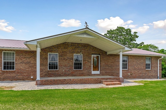 back of property featuring a patio area, brick siding, metal roof, and a lawn