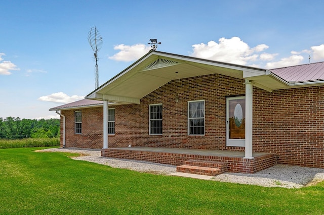 back of property with a yard, a patio area, brick siding, and metal roof