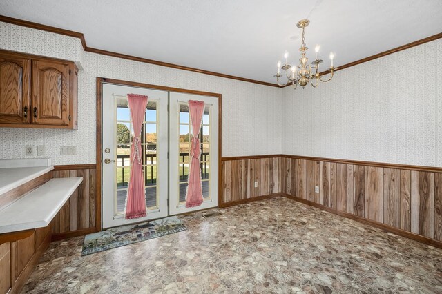 unfurnished dining area with a notable chandelier, a wainscoted wall, visible vents, wallpapered walls, and crown molding