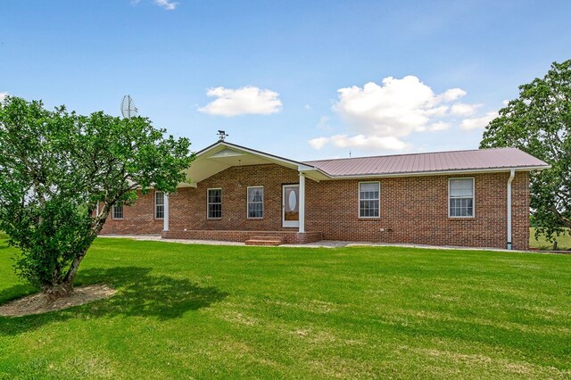 back of house featuring brick siding, metal roof, and a lawn