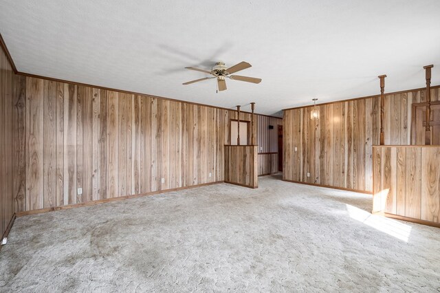 spare room featuring light carpet, baseboards, a ceiling fan, ornamental molding, and wood walls