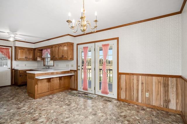 kitchen featuring a wainscoted wall, light countertops, brown cabinetry, a peninsula, and wallpapered walls