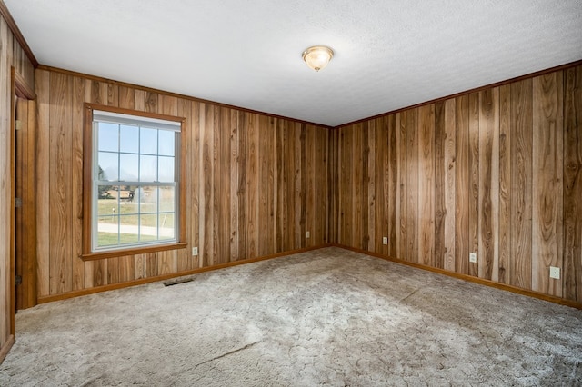 carpeted empty room with visible vents, ornamental molding, wooden walls, a textured ceiling, and baseboards