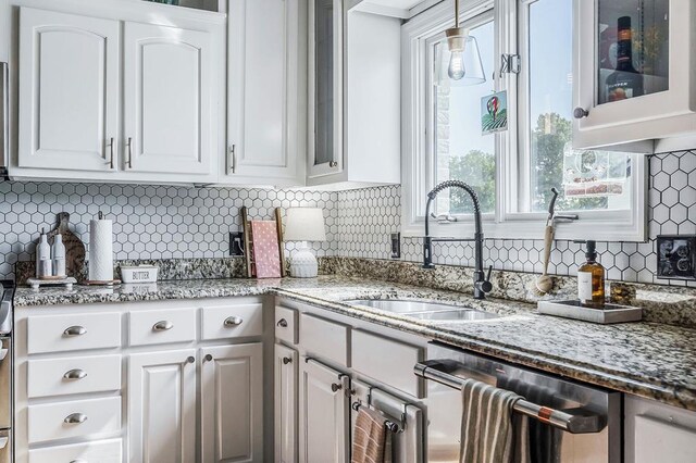 kitchen with stainless steel dishwasher, a sink, glass insert cabinets, and white cabinets