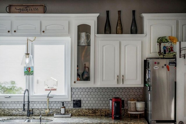 kitchen featuring decorative backsplash, white cabinets, glass insert cabinets, freestanding refrigerator, and a sink