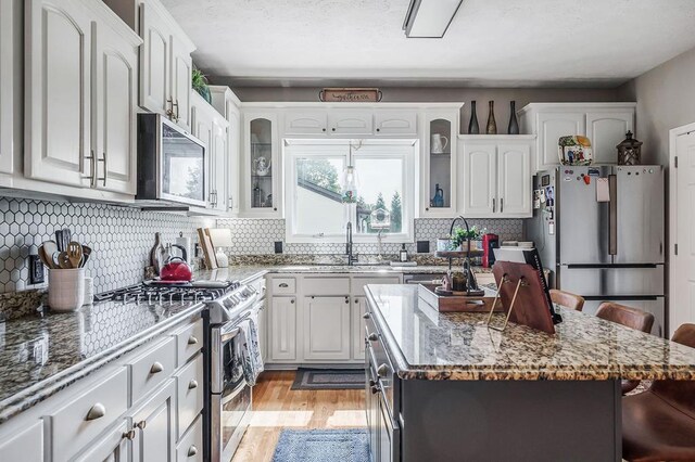 kitchen with white cabinets, a kitchen island, glass insert cabinets, appliances with stainless steel finishes, and a breakfast bar