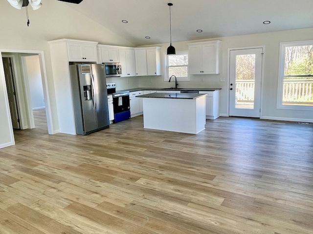 kitchen featuring white cabinets, dark countertops, appliances with stainless steel finishes, decorative light fixtures, and light wood-style floors