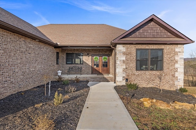 view of exterior entry with roof with shingles, a porch, and brick siding