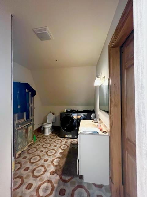 half bath featuring vanity, visible vents, vaulted ceiling, and independent washer and dryer