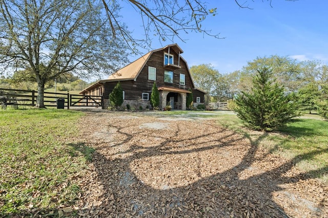 rear view of house with a yard, a barn, a gambrel roof, and fence