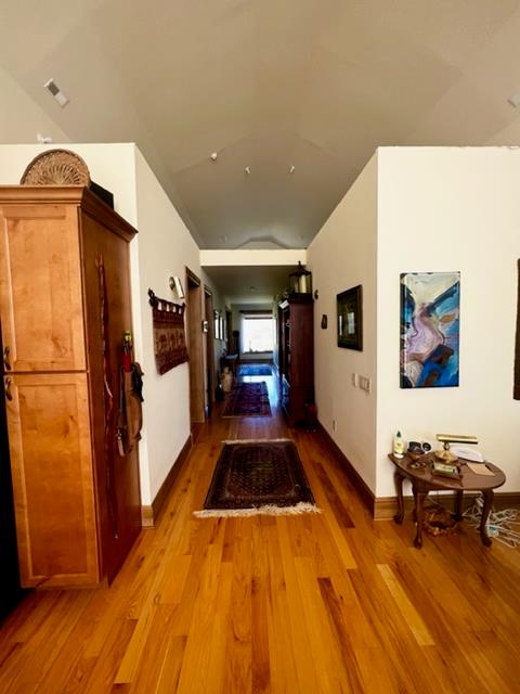 hallway featuring lofted ceiling, visible vents, baseboards, and wood finished floors