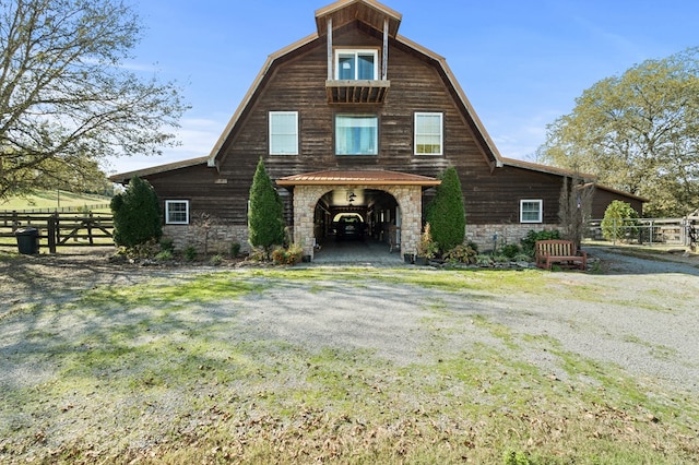 view of front of property with stone siding, fence, and a gambrel roof