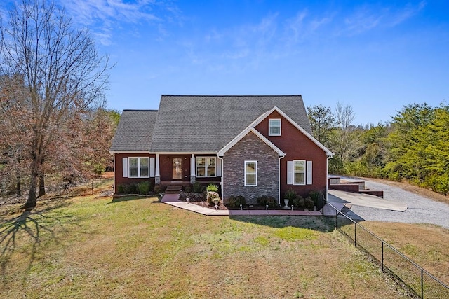 view of front of home featuring stone siding, a shingled roof, fence, and a front yard