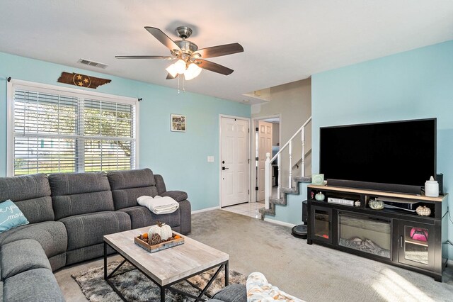 living room with light carpet, visible vents, baseboards, ceiling fan, and stairway