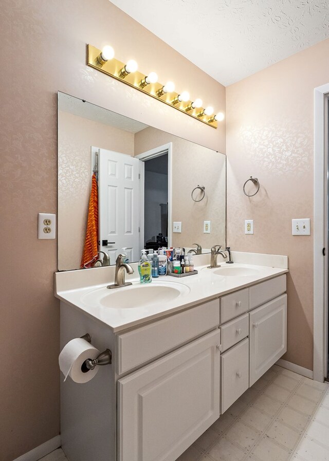 full bath featuring baseboards, double vanity, a sink, and tile patterned floors