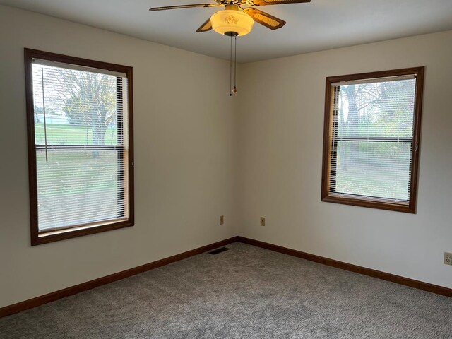 carpeted empty room featuring plenty of natural light, visible vents, baseboards, and ceiling fan