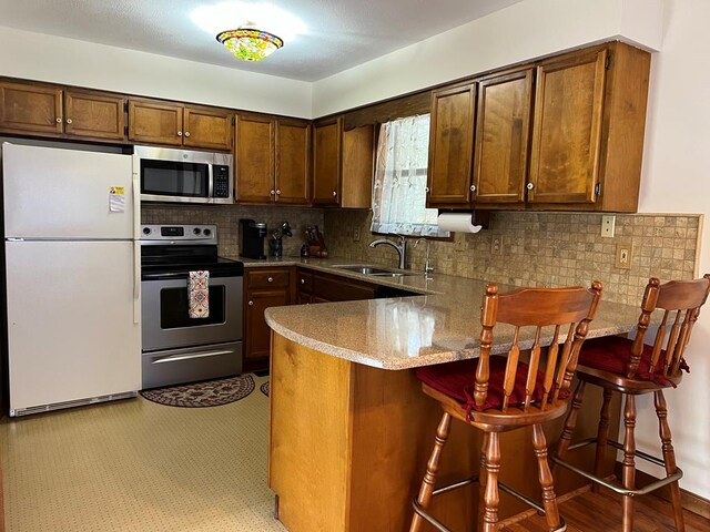 kitchen featuring stainless steel appliances, a sink, a kitchen breakfast bar, light countertops, and decorative backsplash