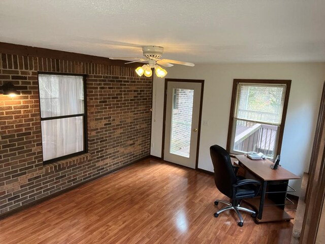 home office with a ceiling fan, brick wall, and wood finished floors