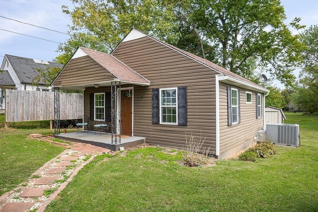 view of front facade with a shingled roof, fence, a front lawn, and central AC