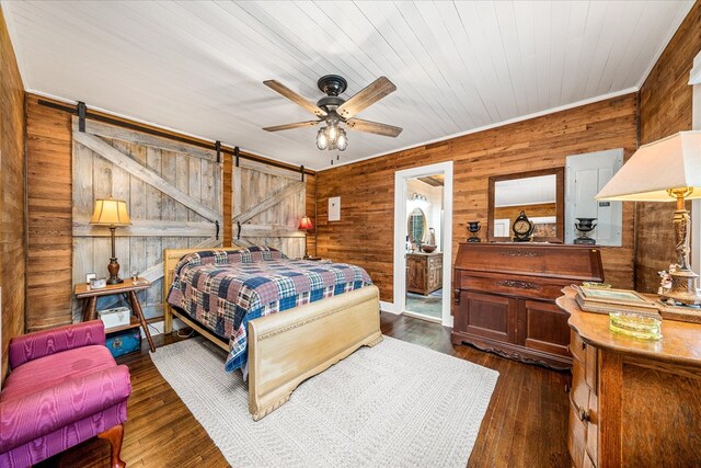 bedroom with dark wood-style floors, ceiling fan, wooden walls, and a barn door