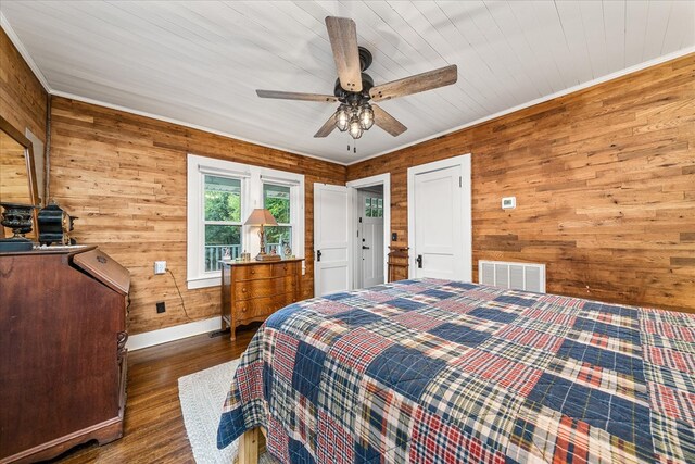 bedroom featuring wooden walls, baseboards, visible vents, dark wood-style floors, and ceiling fan