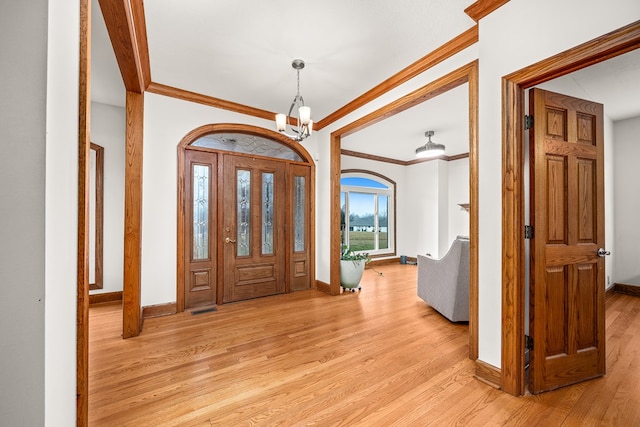 entryway featuring light wood-style flooring, crown molding, baseboards, and a notable chandelier