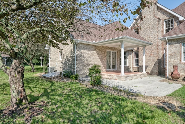 rear view of house featuring brick siding, a lawn, a patio area, and a shingled roof