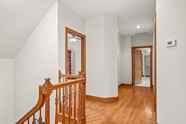 corridor featuring light wood finished floors, baseboards, visible vents, and an upstairs landing