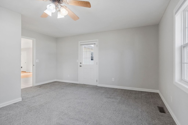 empty room with carpet floors, a healthy amount of sunlight, visible vents, and baseboards