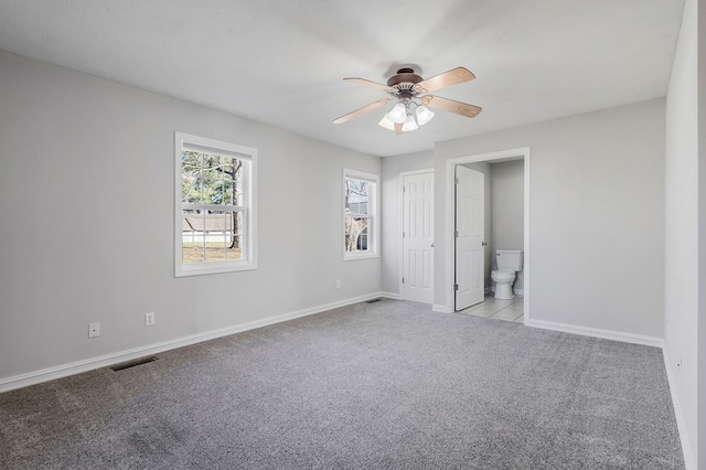 unfurnished bedroom with baseboards, visible vents, connected bathroom, light colored carpet, and ceiling fan