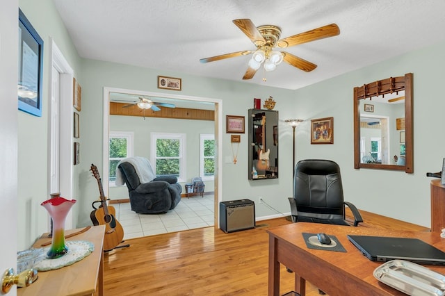 office area featuring ceiling fan, light wood finished floors, a textured ceiling, and baseboards