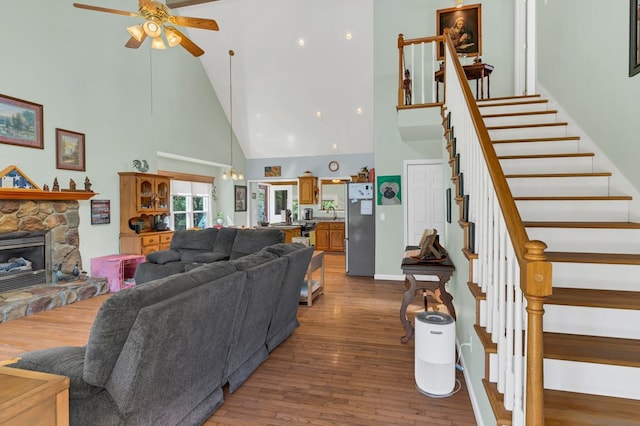 living room with a high ceiling, a fireplace, wood finished floors, a ceiling fan, and stairway