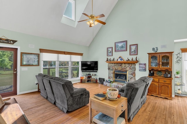 living room with ceiling fan, high vaulted ceiling, a skylight, a fireplace, and light wood finished floors