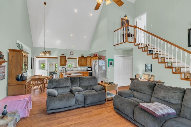 living area featuring a towering ceiling, light wood-style flooring, stairway, and ceiling fan with notable chandelier