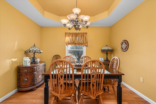 dining area with baseboards, wood finished floors, a raised ceiling, and an inviting chandelier