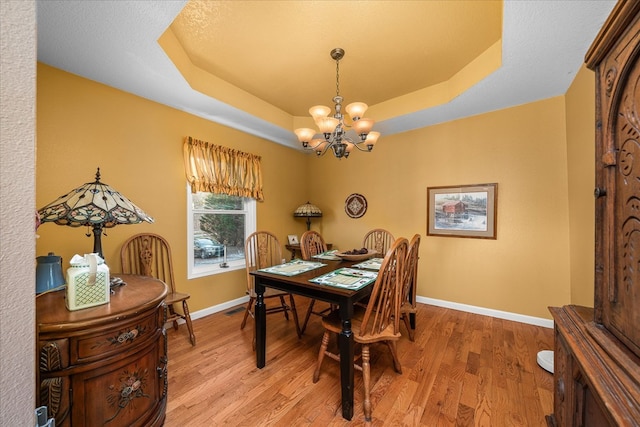 dining space with a raised ceiling, a notable chandelier, baseboards, and wood finished floors