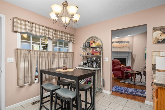 dining room featuring light tile patterned floors, a textured ceiling, a chandelier, baseboards, and a lit fireplace