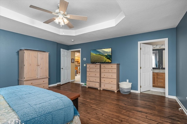 bedroom featuring dark wood-style floors, a raised ceiling, a sink, a textured ceiling, and baseboards