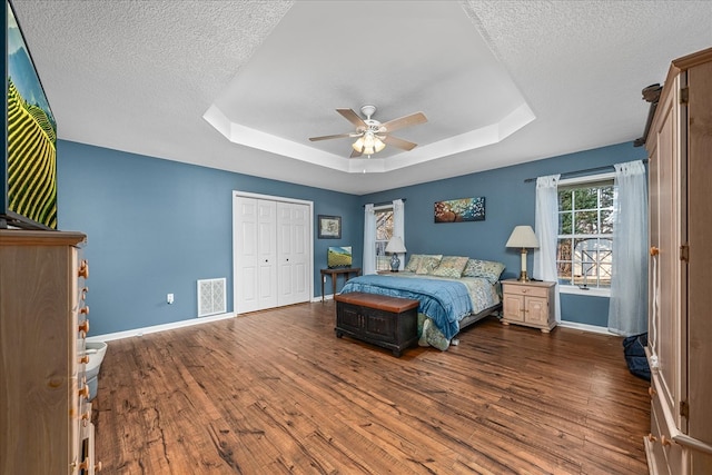 bedroom featuring dark wood-style floors, baseboards, visible vents, and a raised ceiling