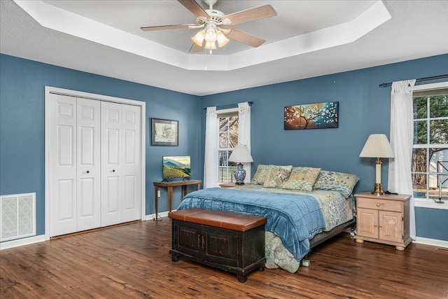 bedroom featuring dark wood-style floors, a raised ceiling, visible vents, and a closet