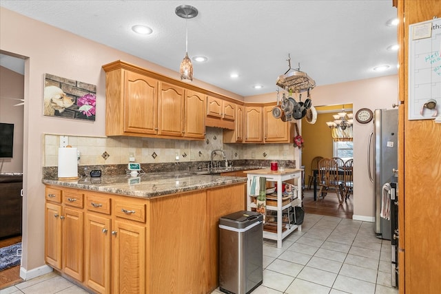 kitchen with dark stone counters, freestanding refrigerator, a sink, backsplash, and light tile patterned flooring