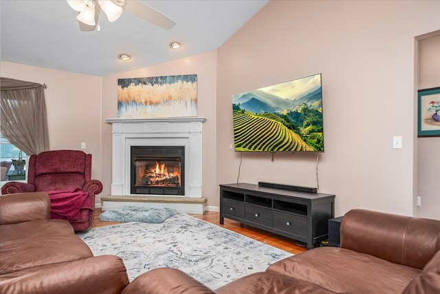 living room with lofted ceiling, light wood-type flooring, a ceiling fan, and a glass covered fireplace