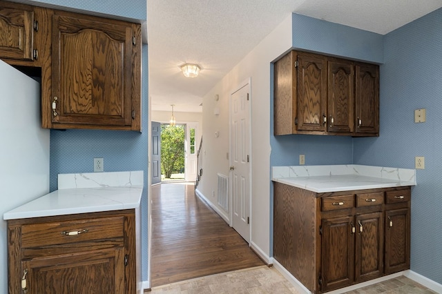 kitchen featuring a textured ceiling, light countertops, dark brown cabinetry, and wallpapered walls