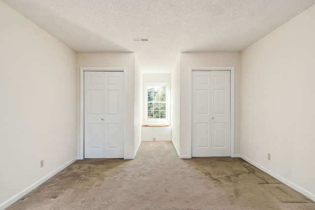 unfurnished bedroom with visible vents, baseboards, light colored carpet, a textured ceiling, and multiple closets