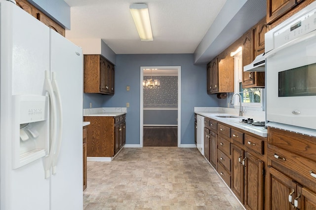 kitchen with white appliances, brown cabinetry, light countertops, under cabinet range hood, and a sink